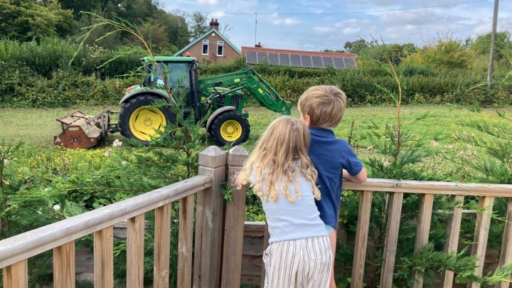 Children watching a tractor from the garden at Blackfirs Farmhouse in Battle, East Sussex