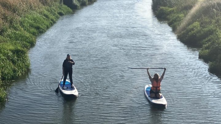 Two people paddleboarding on a countryside waterway near Battle, East Sussex